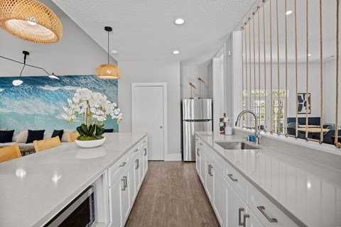 A kitchen with white cabinets and a painting of a blue ocean on the wall.