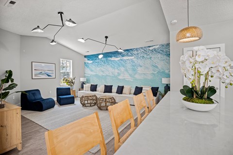 A living room with a blue couch and a large painting of a wave on the wall.