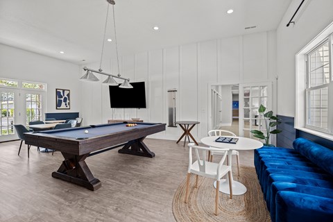 A pool table with a blue cloth and a television on the wall.