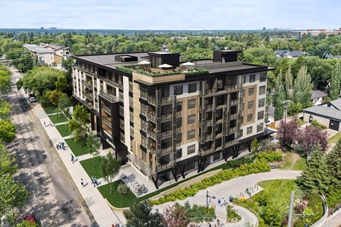 A large building with balconies and plants on the roof is surrounded by a green lawn and trees.