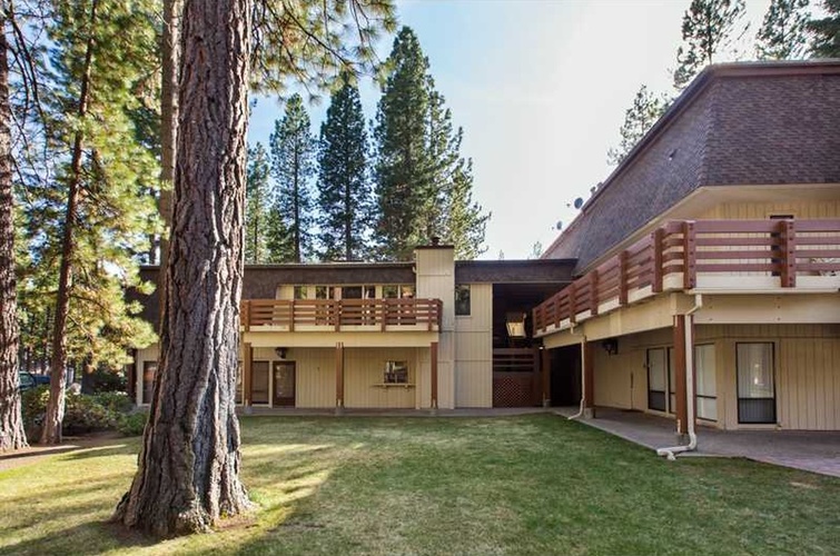 A house with a brown roof and a balcony is surrounded by trees.