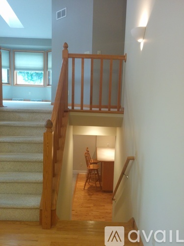 A wooden staircase with a carpeted runner leads up to a landing with a chair and a table.