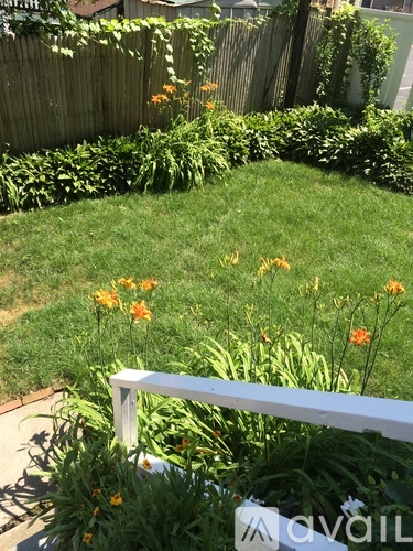 A white fence in a garden with green grass and orange flowers.