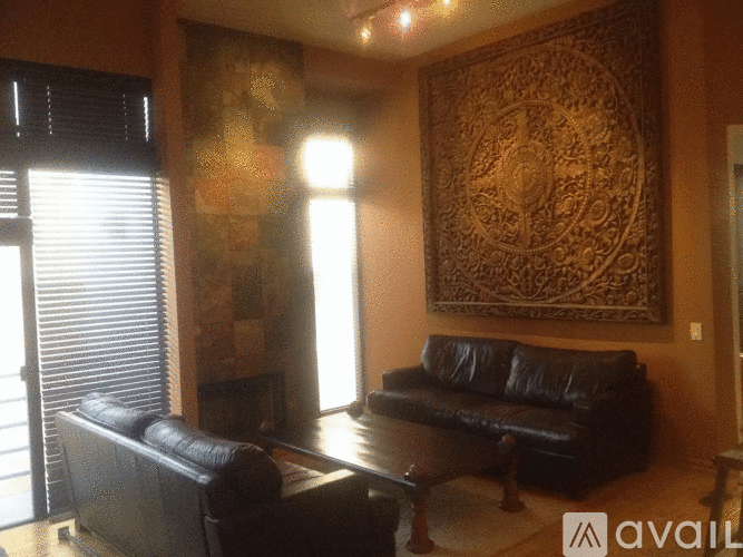 A living room with a black leather couch and a large tapestry on the wall.