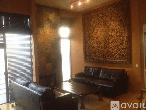 A living room with a black leather couch and a large tapestry on the wall.