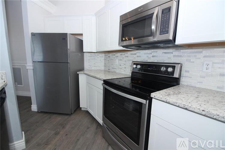 A kitchen with a stainless steel refrigerator, black stove, and white cabinets.