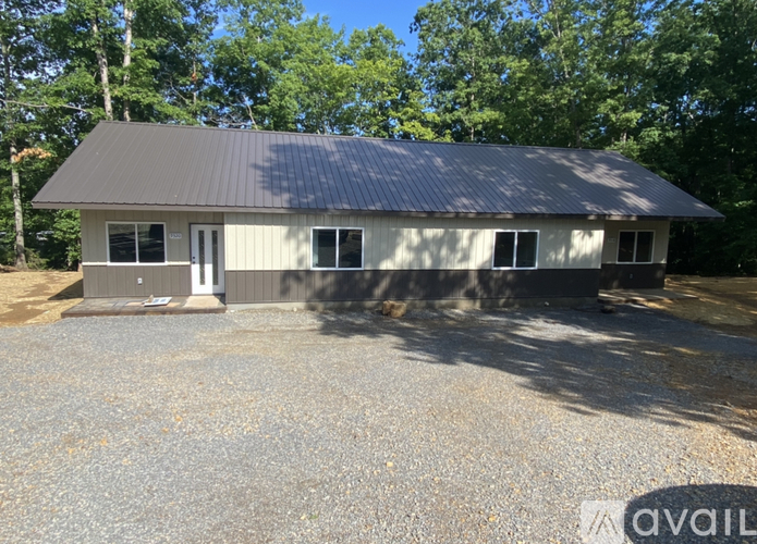 A house with a grey roof and white walls is surrounded by trees.