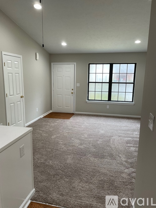 A carpeted room with a window and two doors.