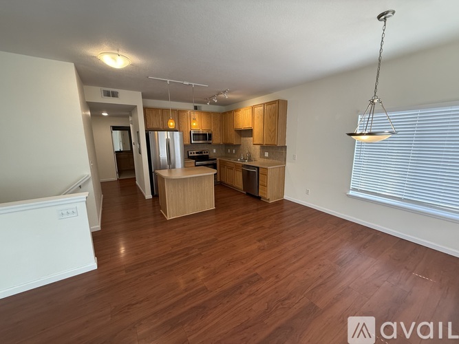 A spacious living room with wooden flooring and a kitchen area in the background.