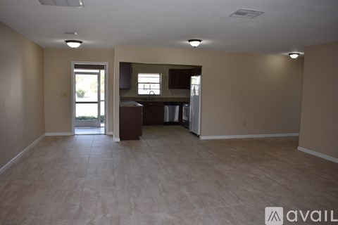A spacious room with beige walls and light brown flooring, featuring a kitchenette with a sink and a refrigerator.
