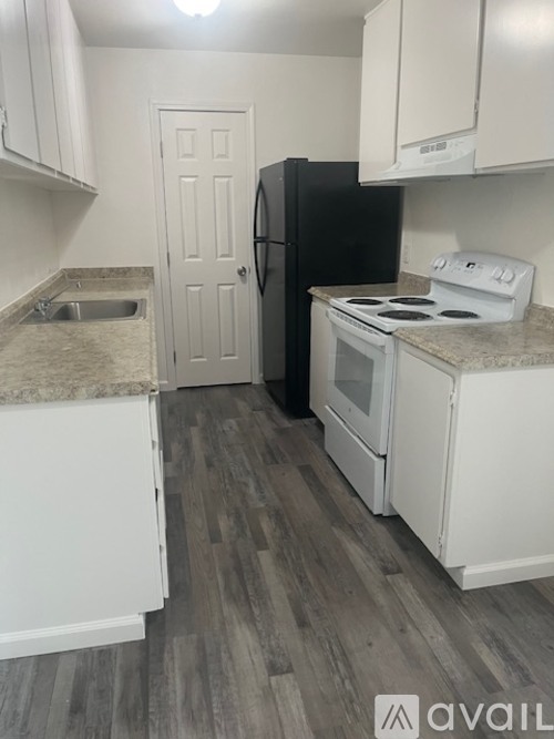 A kitchen with a black refrigerator, white cabinets, and a stove top oven.