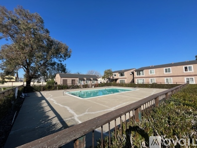 A pool surrounded by a fence and trees in front of apartment buildings.