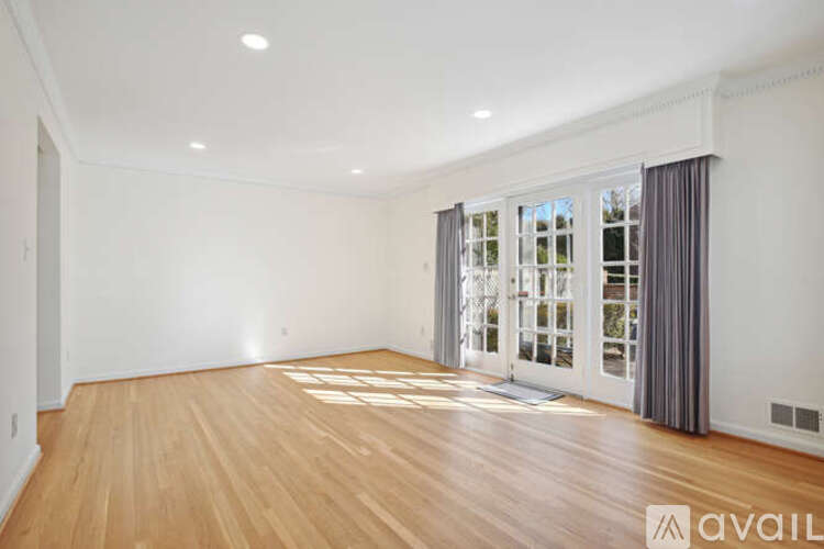 A spacious room with wooden flooring and a large window with curtains.
