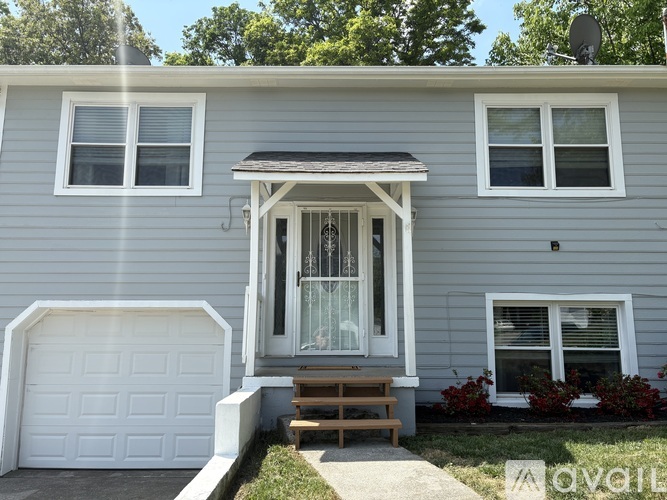 A grey house with a white garage door and a wooden bench in front of the door.