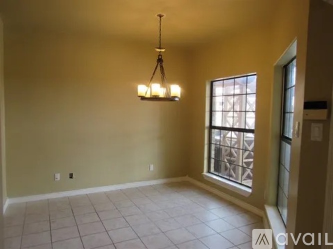 A room with a chandelier, tiled floor, and a window with a view of a balcony.