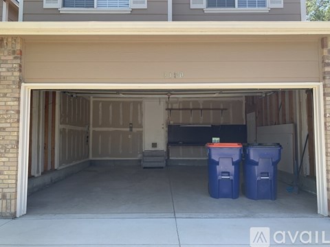 A garage with two blue bins in front of it.