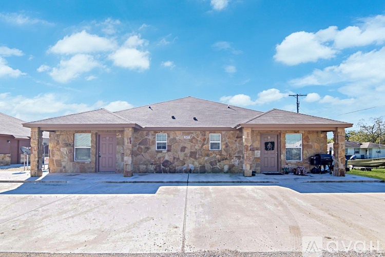 A house with a brown roof and a stone exterior is surrounded by a concrete driveway.