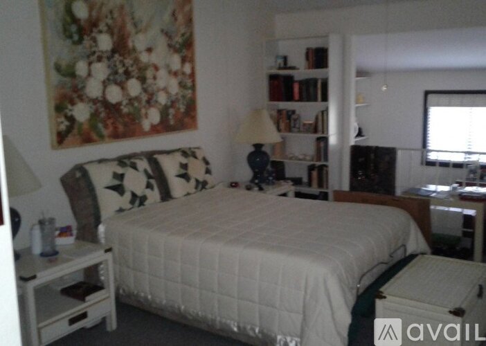 A bedroom with a bed, nightstand, and a painting on the wall.