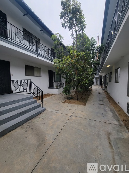 A white building with a black railing and a tree in front.