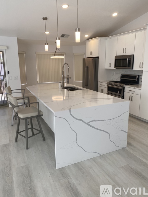 A modern kitchen with a marble island and pendant lights.