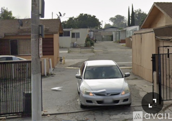 A silver car is parked on a street with houses on either side.