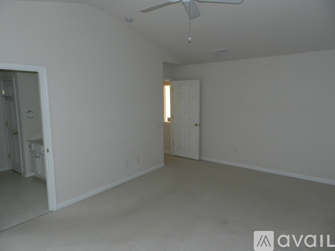 A spacious empty room with a ceiling fan and a door leading to another room.