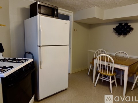 A white refrigerator is in a kitchen with a black stove and a table with chairs.