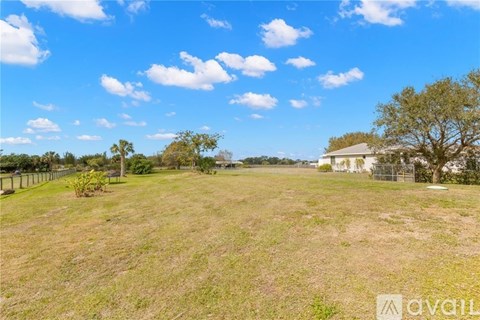 A large, open field with a house and trees in the distance under a blue sky.