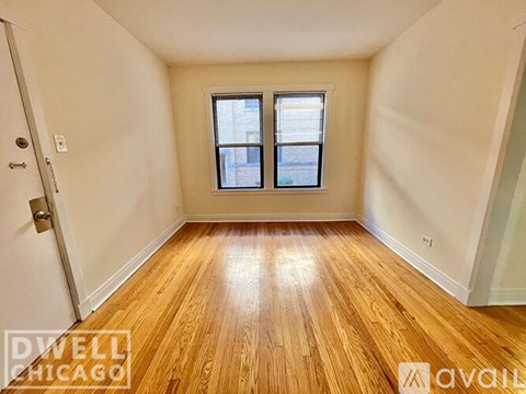 A room with wooden flooring and a window with a view of a building outside.