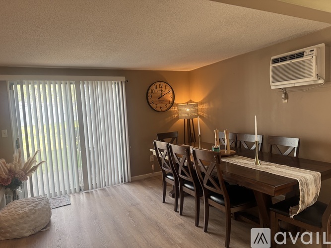 A dining room with a wooden table and chairs, a clock on the wall, and a vase with flowers on the table.