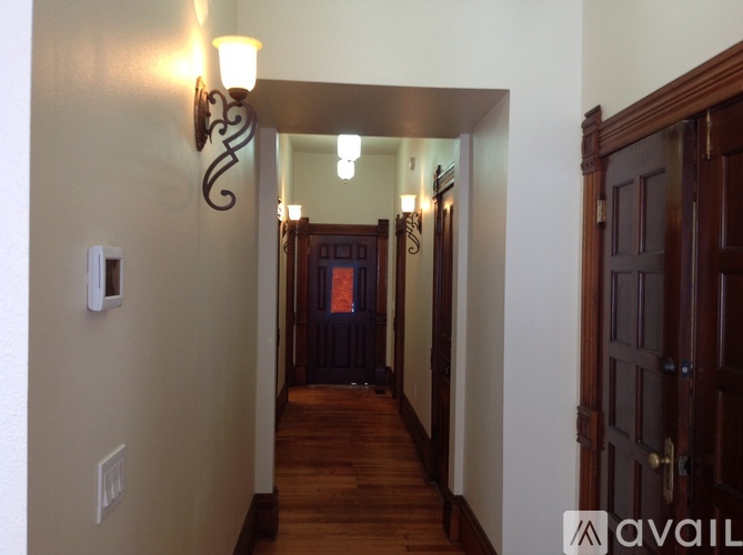 A hallway with a light fixture on the wall and a door at the end.