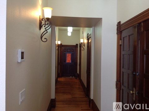 A hallway with a light fixture on the wall and a door at the end.