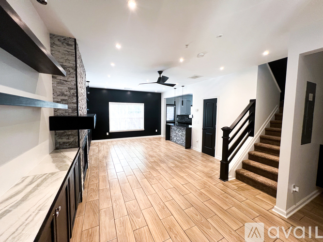 A spacious room with wooden flooring and a staircase.