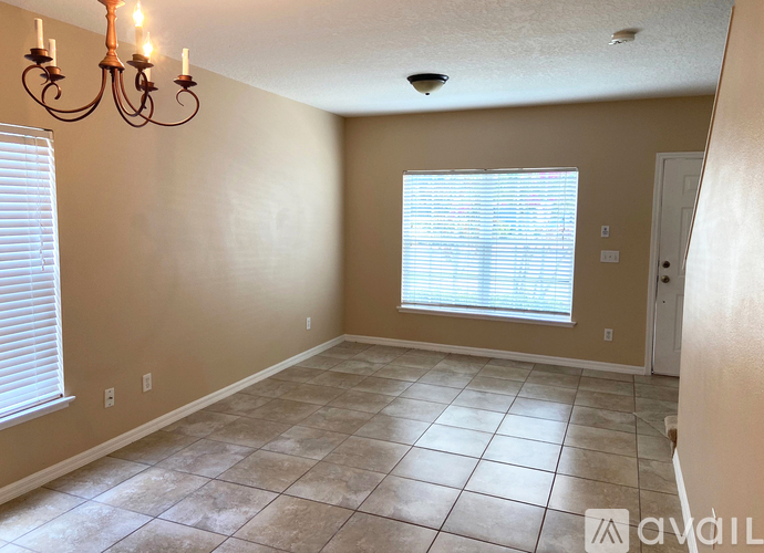 A room with a chandelier, tiled floor, and a window with blinds.