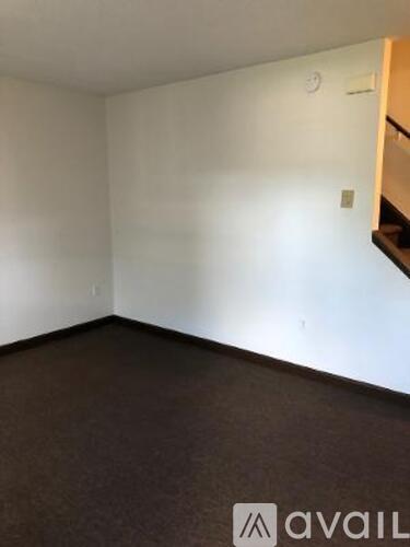 A room with a carpeted floor and a staircase in the background.