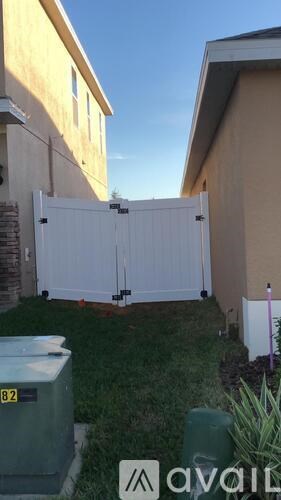 A white gate is closed in front of a tan building.