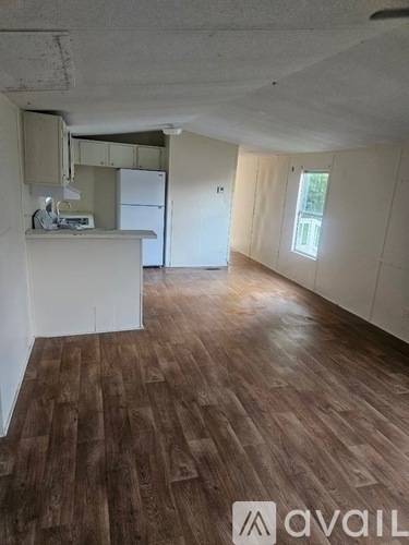 A room with wooden flooring and white walls, with a kitchenette and a window.