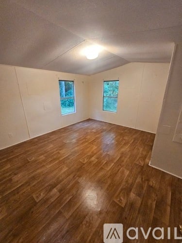 A room with wooden flooring and two windows.
