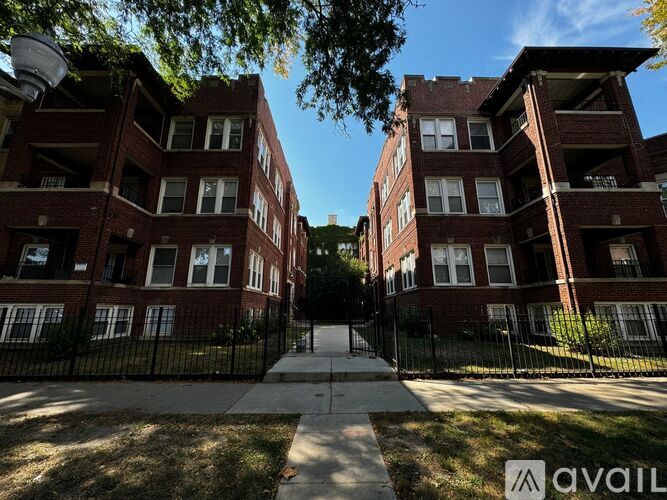 A row of red brick apartment buildings with black fencing and a sidewalk in front.