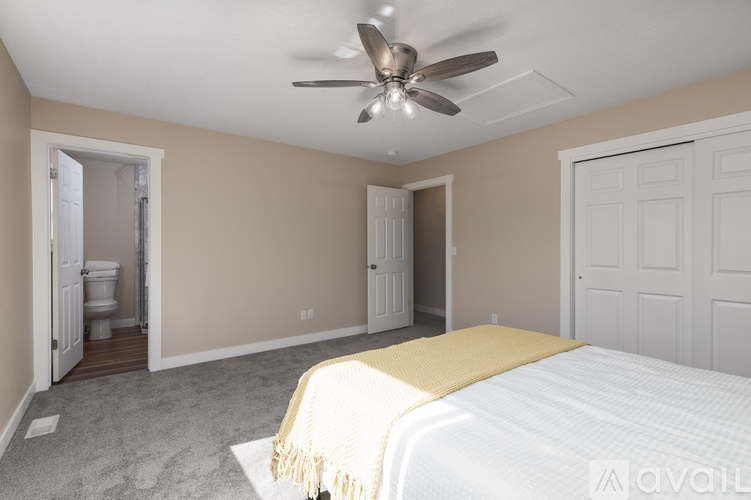 A bedroom with a bed, a ceiling fan, and a toilet visible through an open door.