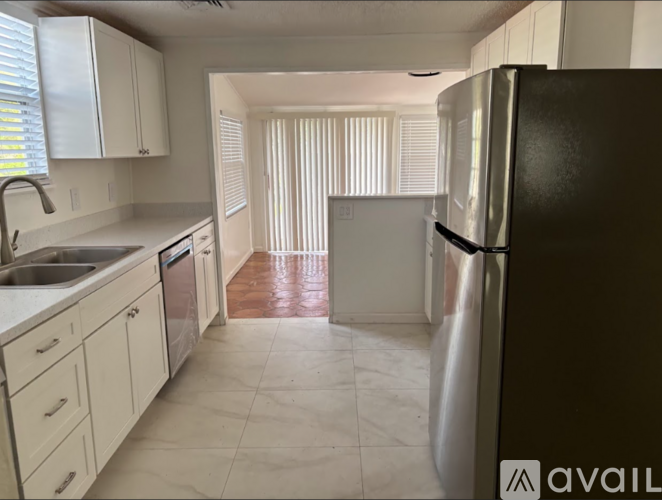 A kitchen with a black refrigerator, white cabinets, and a marble floor.