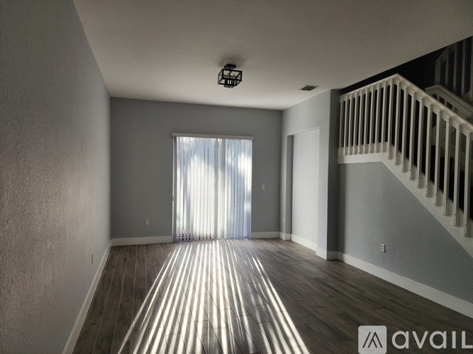 A spacious room with wooden floors and a staircase on the right side.
