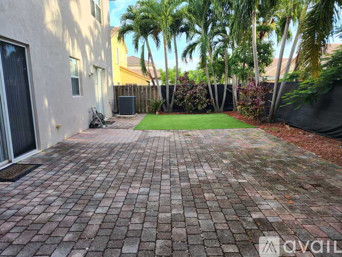 A patio with a brick pattern is surrounded by a fence and trees.