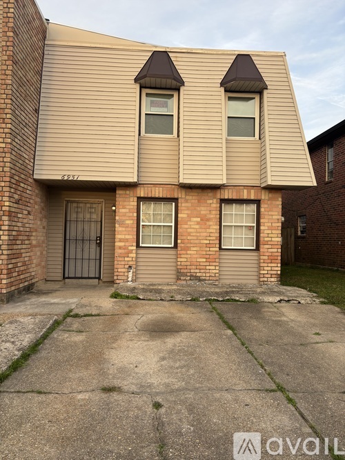A house with a brown siding and a brick facade has a black gate and a small front yard.