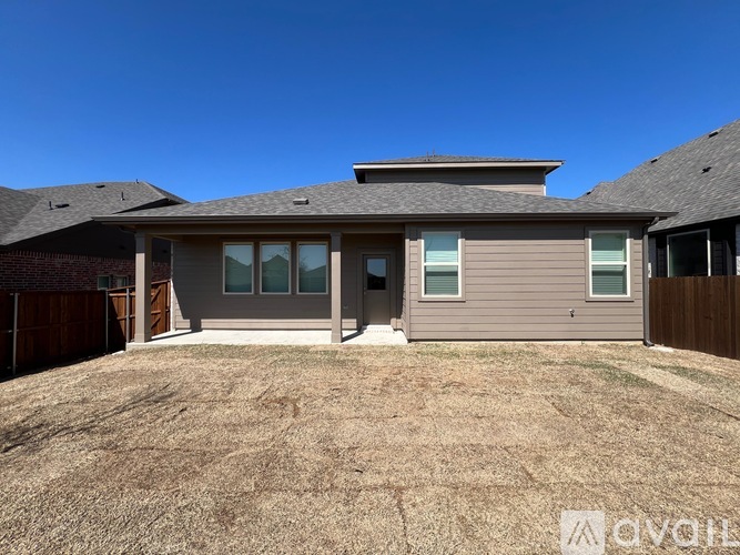 A house with a brown roof and grey siding is surrounded by a dry grassy area.