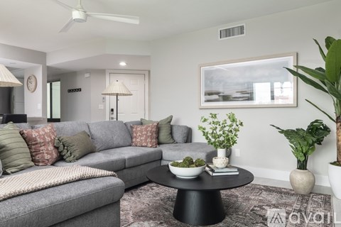 A living room with a grey couch, a black coffee table, and a painting on the wall.