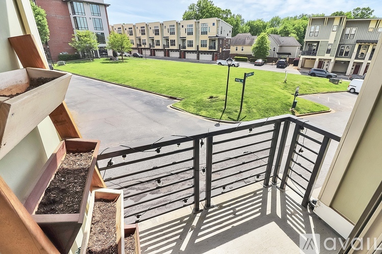 A balcony view of apartment buildings with a green lawn and trees in the background.