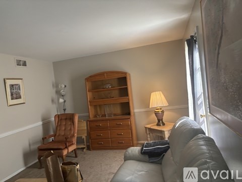 A living room with a grey couch, a brown chair, a wooden bookcase, and a lamp on a side table.