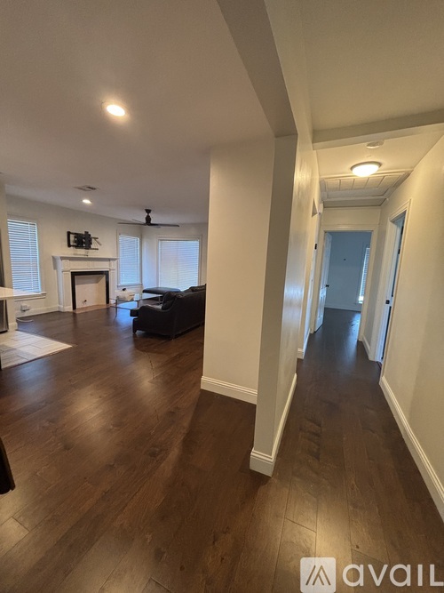 A hallway with wood floors and white walls leading to a door.