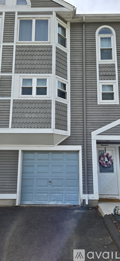 A grey house with a white door and a window with a wreath on it.